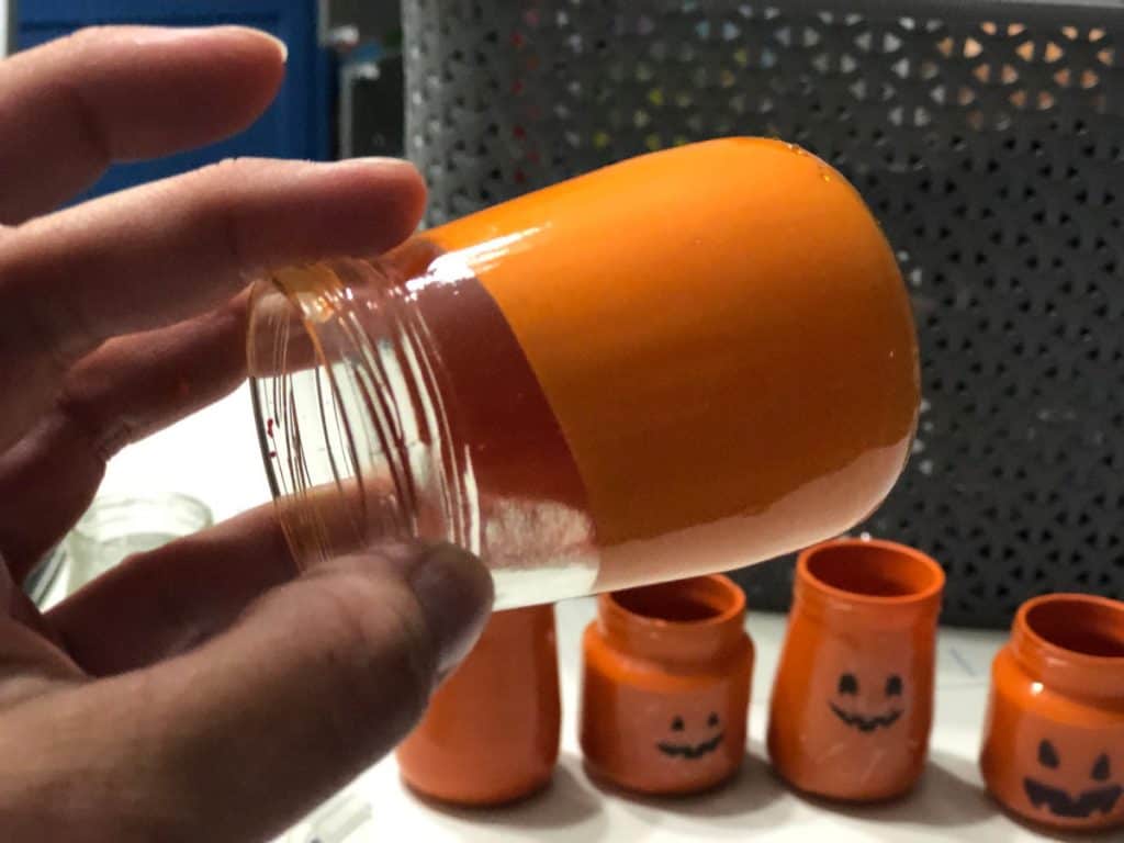 Clear jar tilted on side with paint inside moving around to coat inside of jar almost done