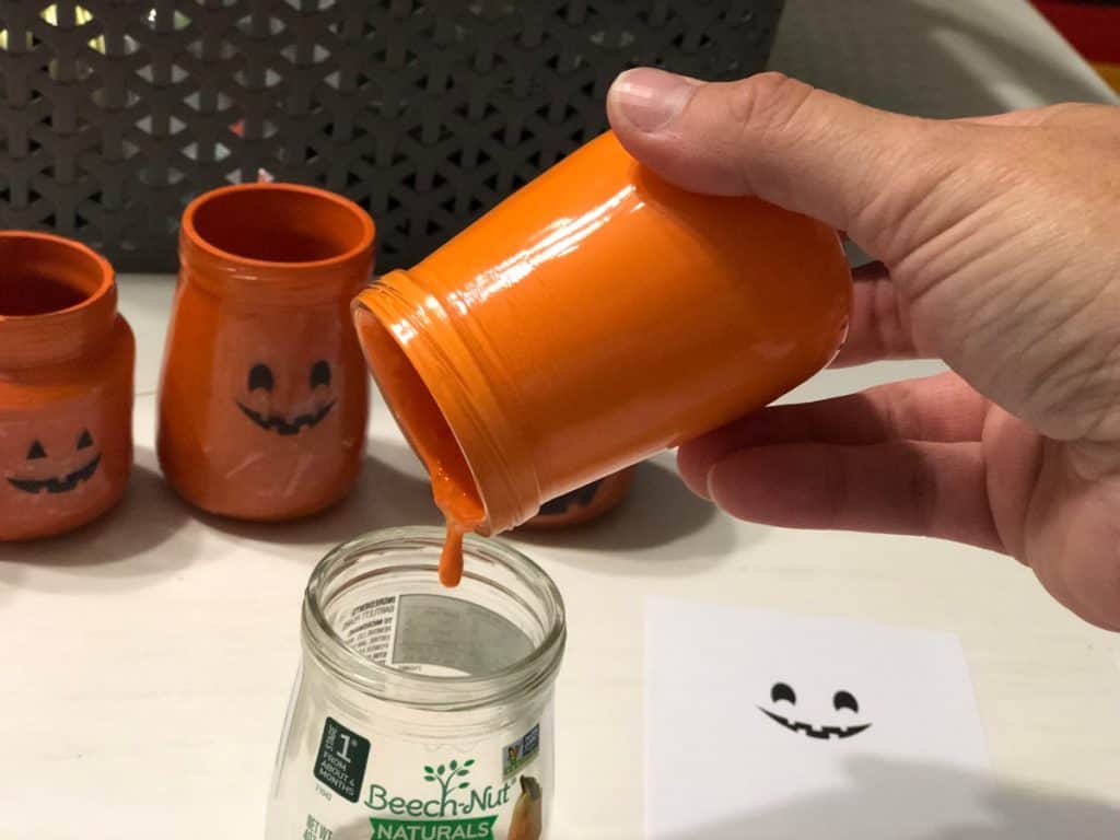 leftover Paint pouring from an orange painted jar to a leftover clear unused jar