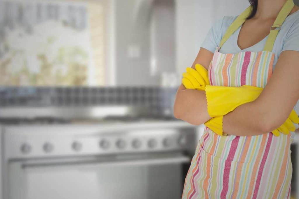 Woman in a kitchen wearing cleaning gloves and an apron