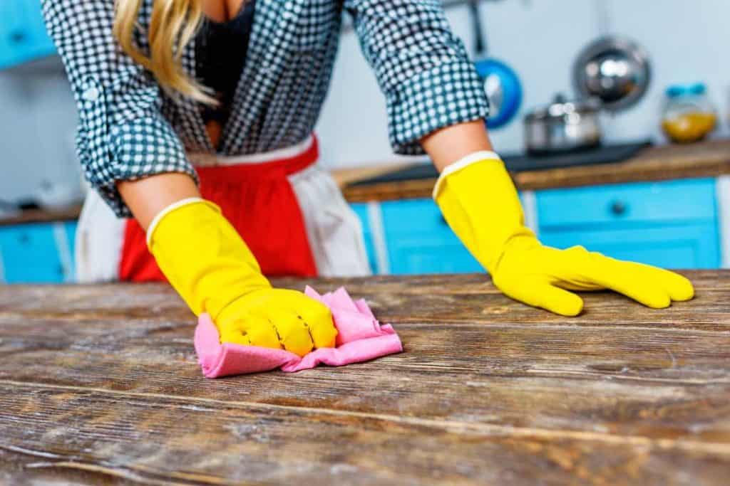 Lady scrubbing down countertops with gloves and a sponge.