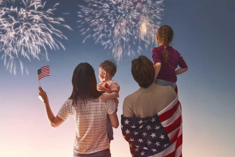 A family watching fireworks, a mom holding a baby and a dad holding a young girl.
