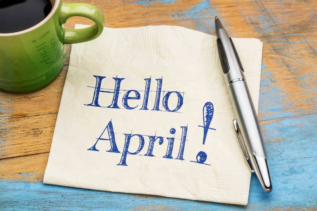 Hello April written on a napkin with a pen on a wooden table with a cup of coffee on the side