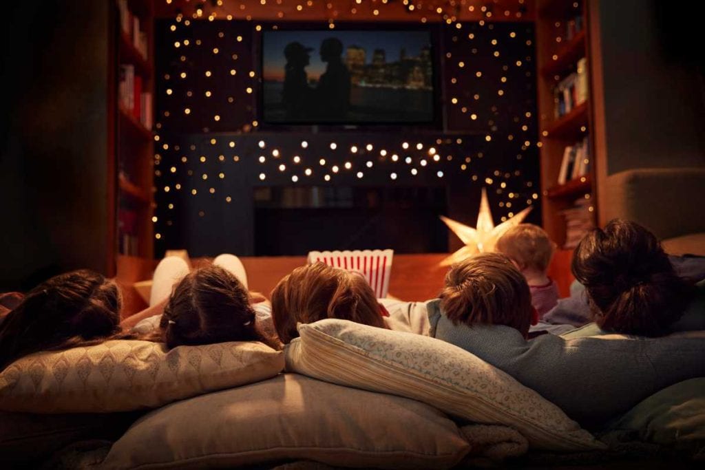 A family snuggled up on the couch at night with lights strung around for a movie night