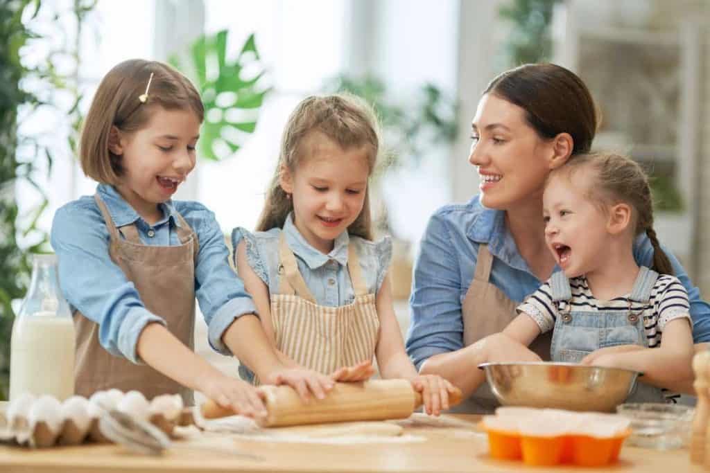Mom with three daughters baking and rolling out dough with a rolling pin
