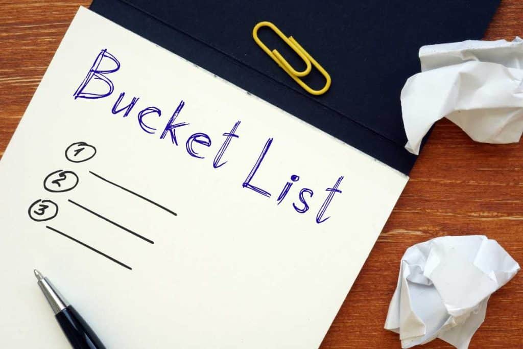 Notebook with a bucket list outline written on it with wadded up paper and paperclips and a pen