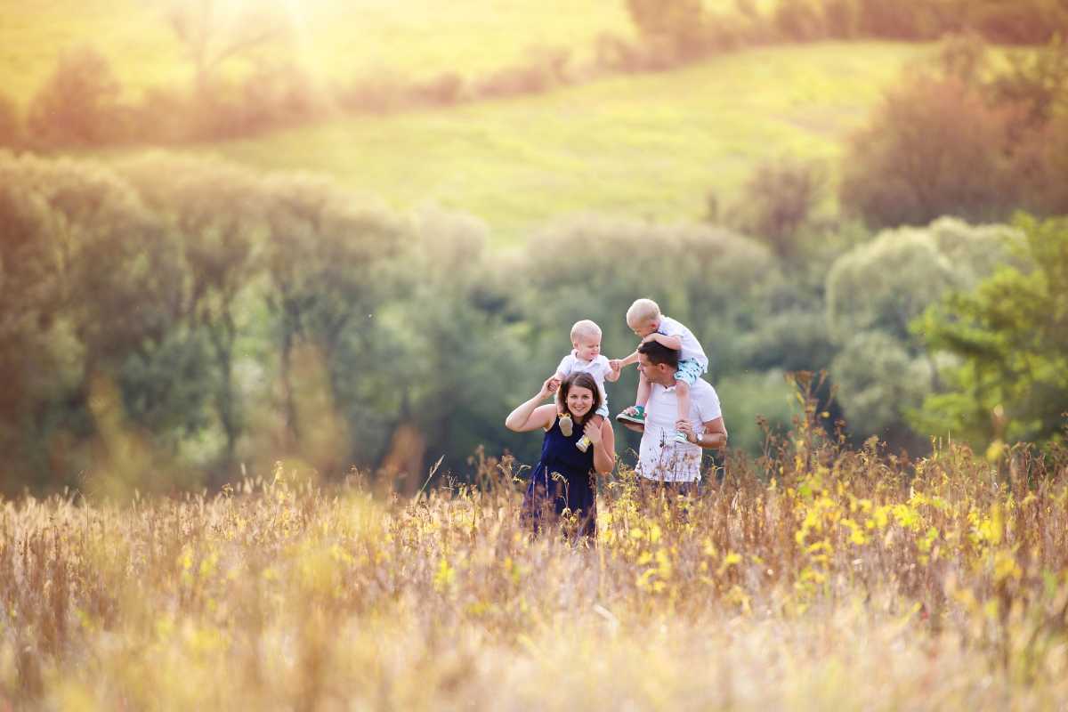 A mom and dad on a walk in a field with their two kids on their shoulders