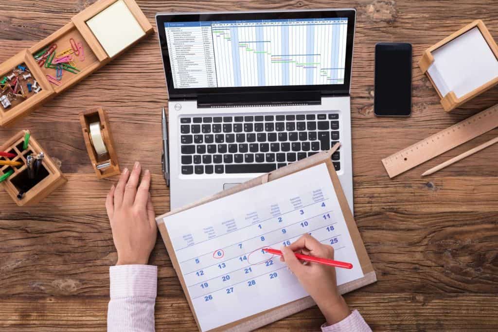 Woman working at a computer on a desk with a paper calendar and red pen in her hand