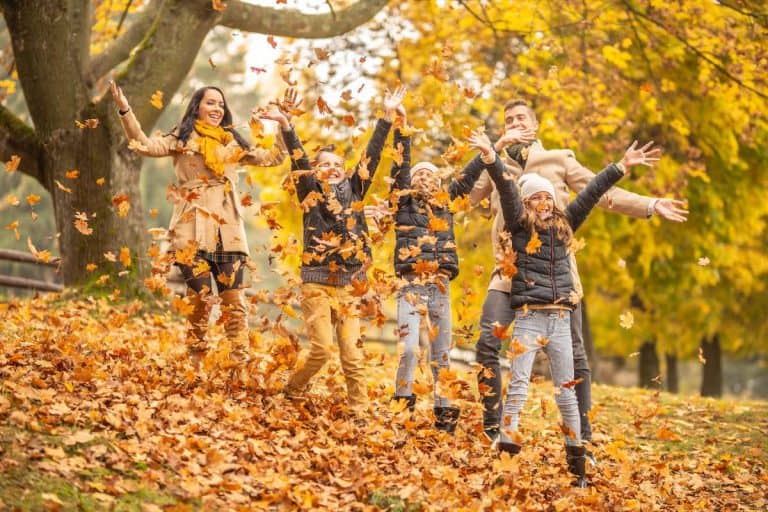 Mom and Dad and 3 kids throwing leaves in the air and smiling for the camera during the Fall season