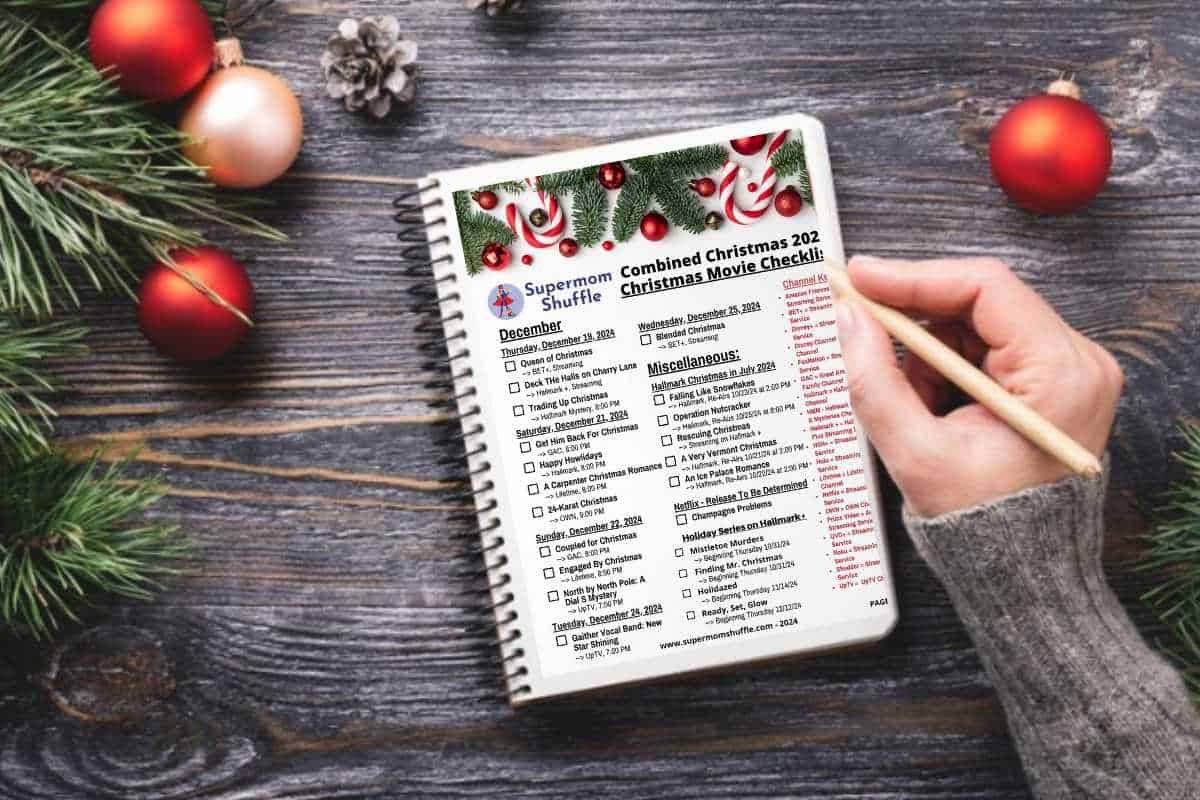 The Supermom Shuffle Printable Christmas movie list on a table with a woman checking off movies and Christmas decorations lying all across the table.