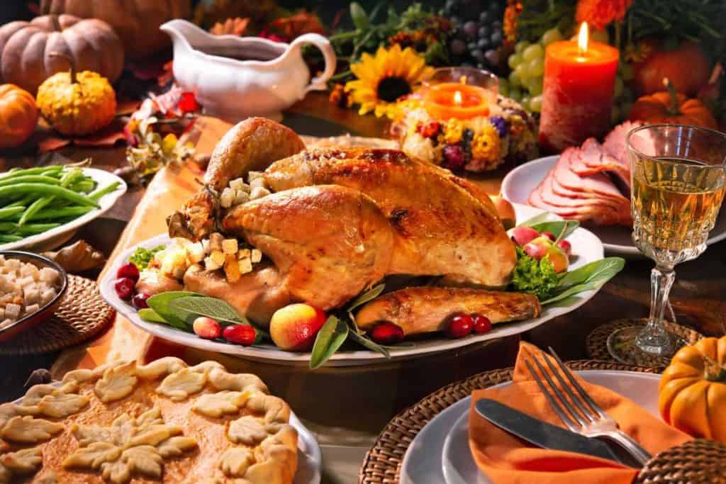 Thanksgiving feast on a table with the roasted turkey in the center, surrounded by pie, green beans and ham and gravy.