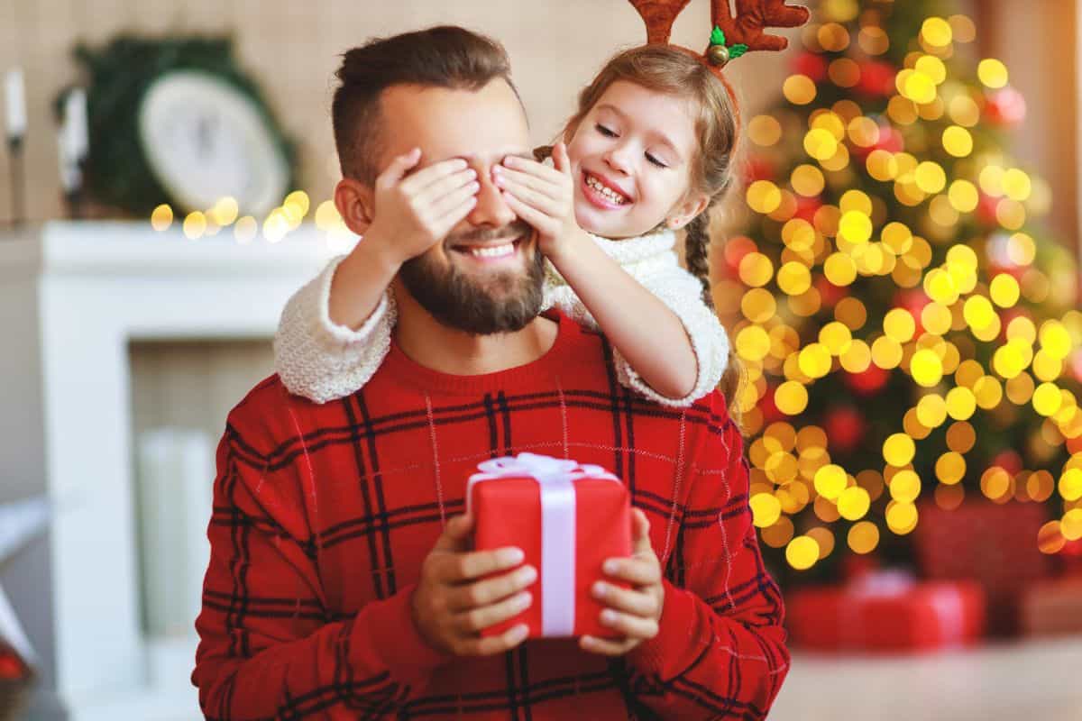 Little girl covering her dad's eyes to surprise him with a present