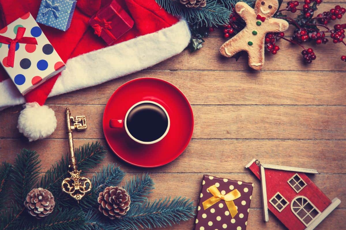 Red cup of coffee on a red saucer on a wooden table that has Christmas decorations strewn all around