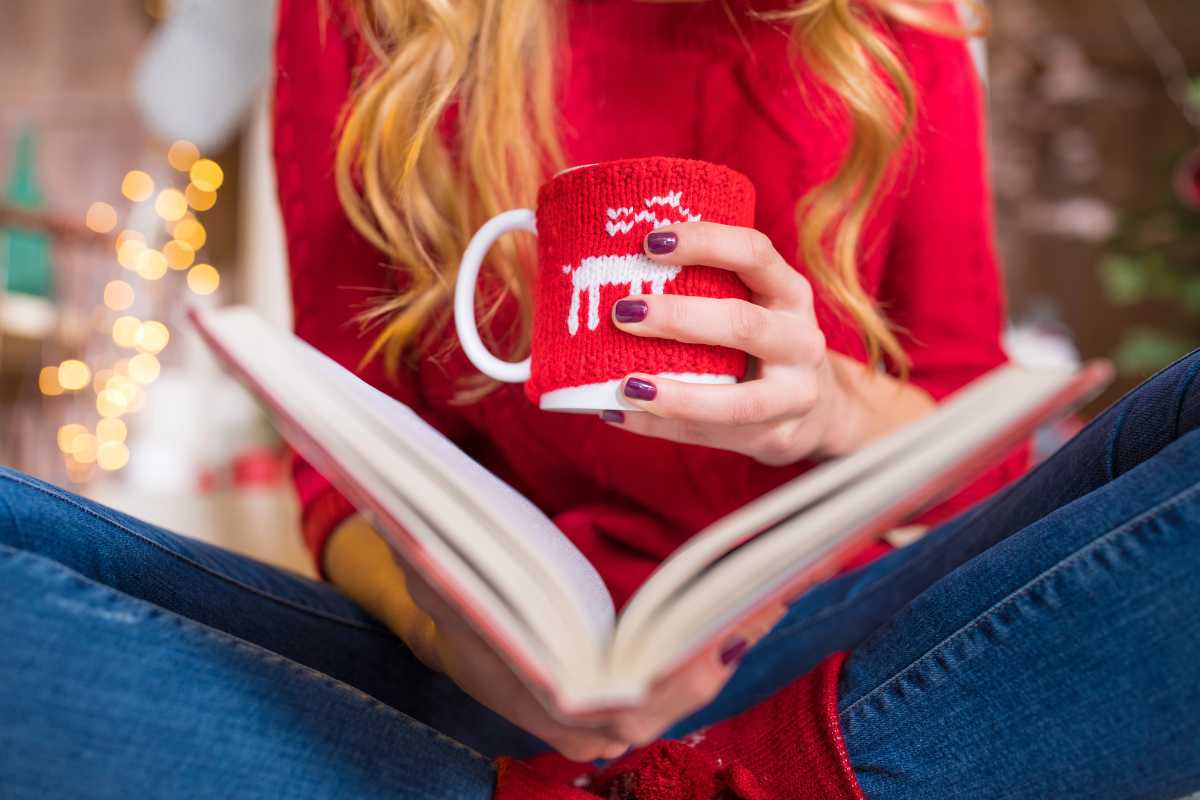 Woman reading a Christmas book while holding a warm mug of cocoa.