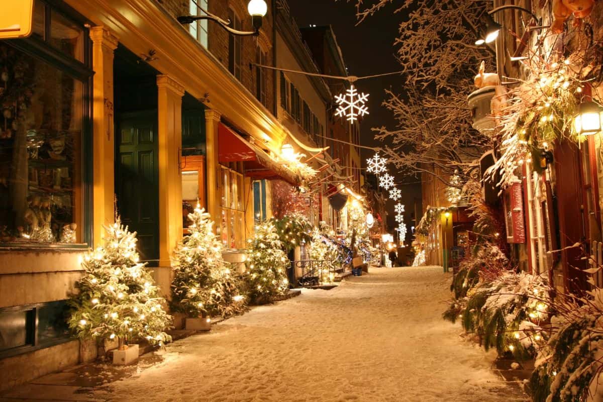 City street lit up at night and decorated for Christmas with snow on the ground.