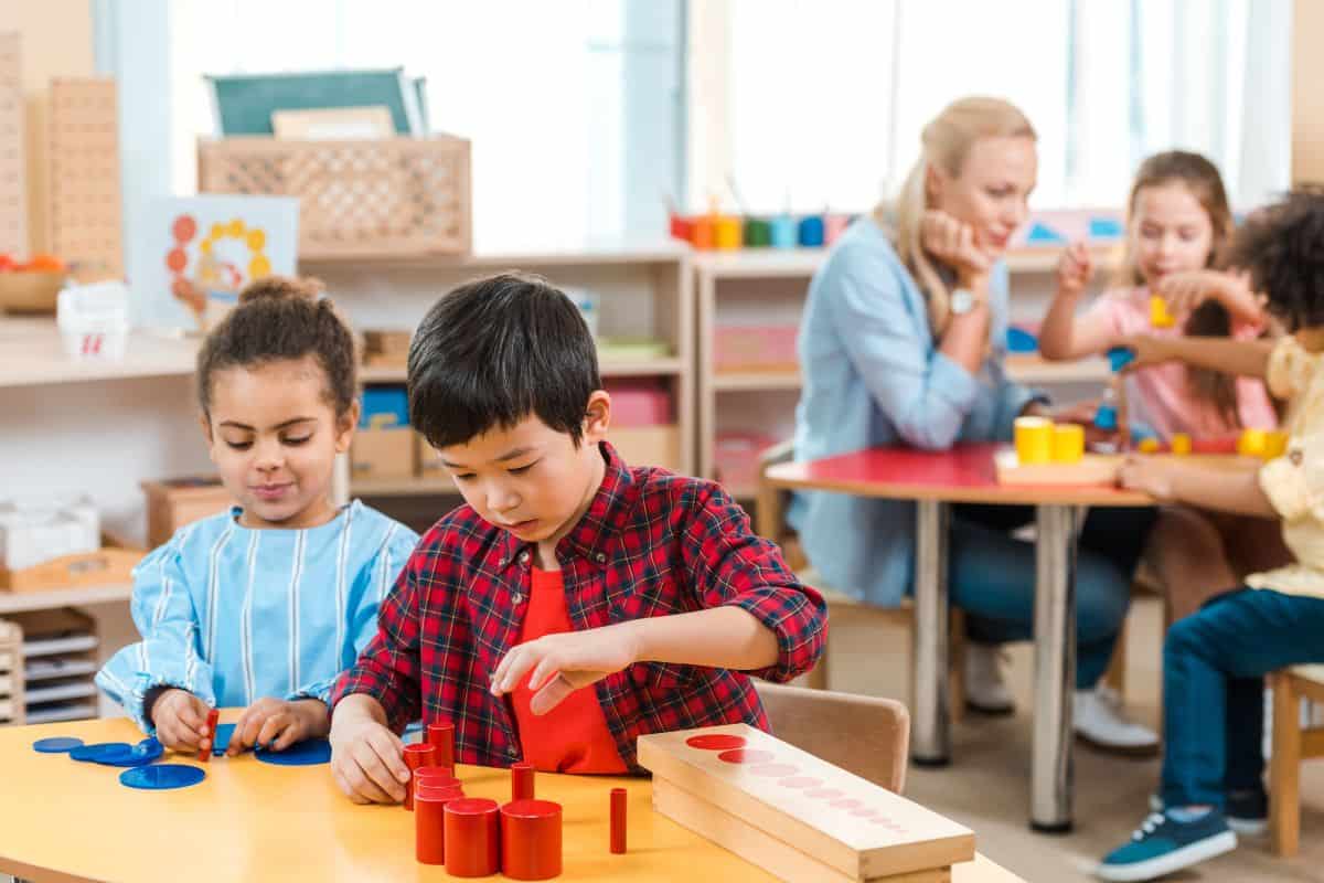 Preschool classroom with kids sitting at tables doing learning activities with a teacher sitting with them