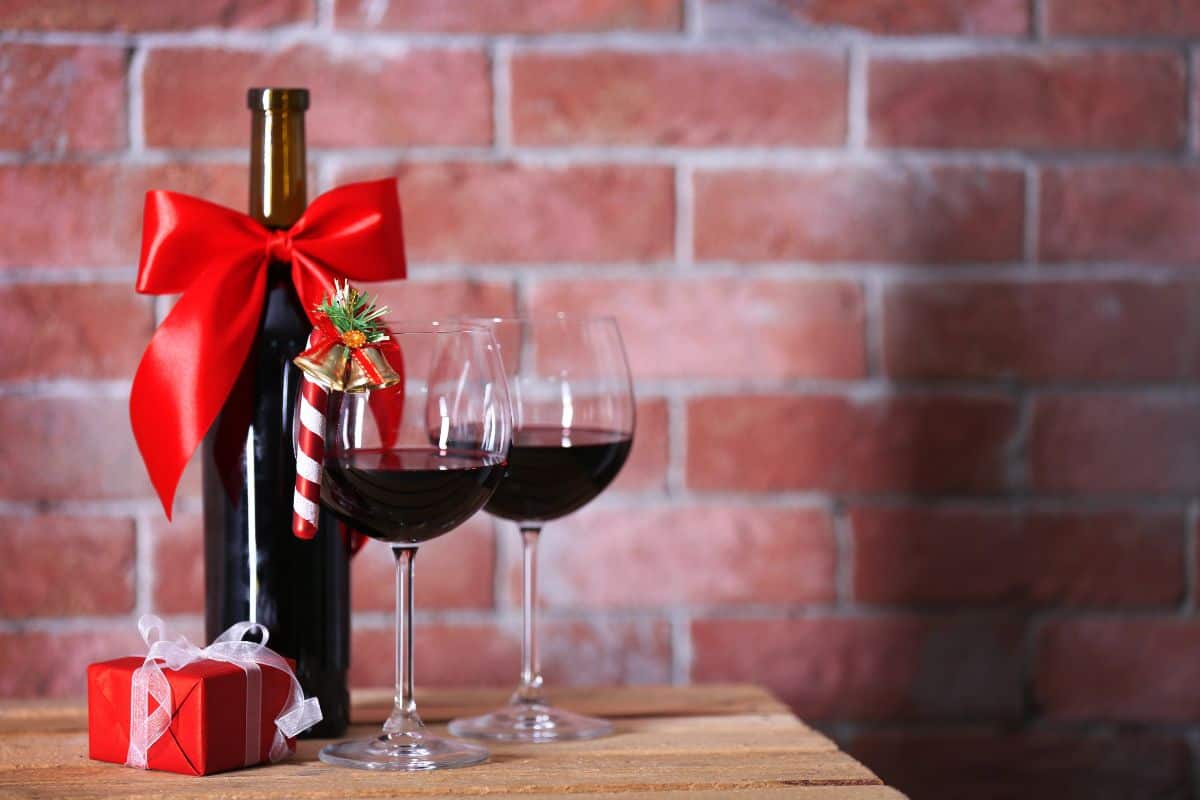 Two glasses of red wine with candy cane Christmas decorations on them with a bottle of red wine next to the glasses with a red bow on it.