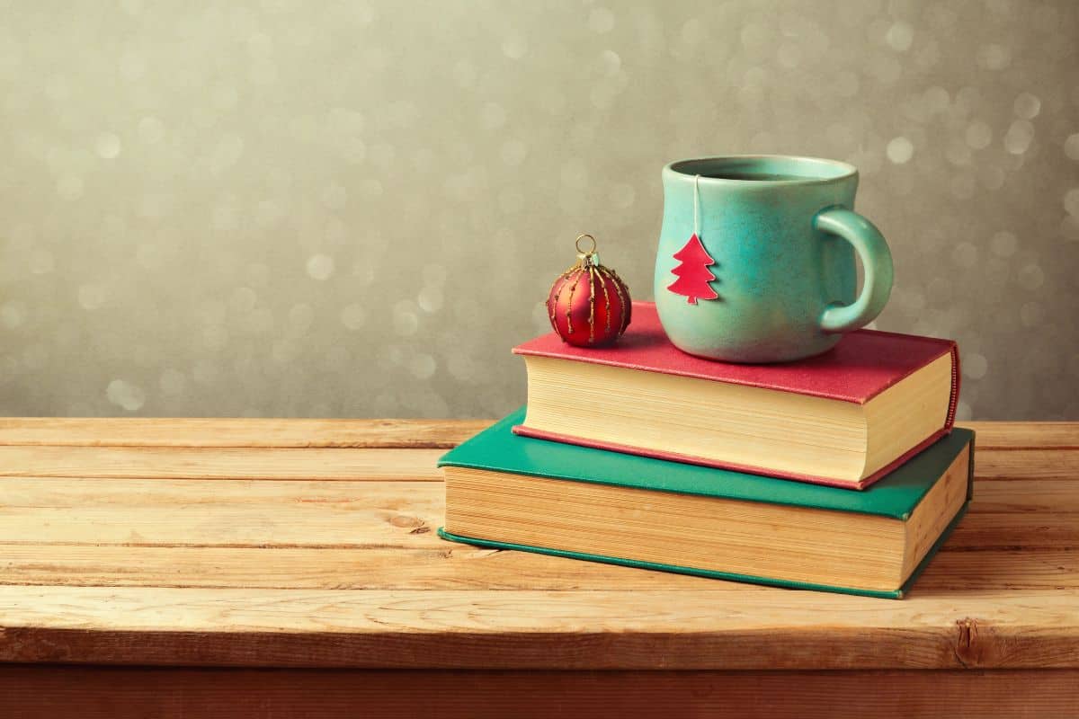 Two books on a wooden bench with a teacup on top with a christmas tree and ornament