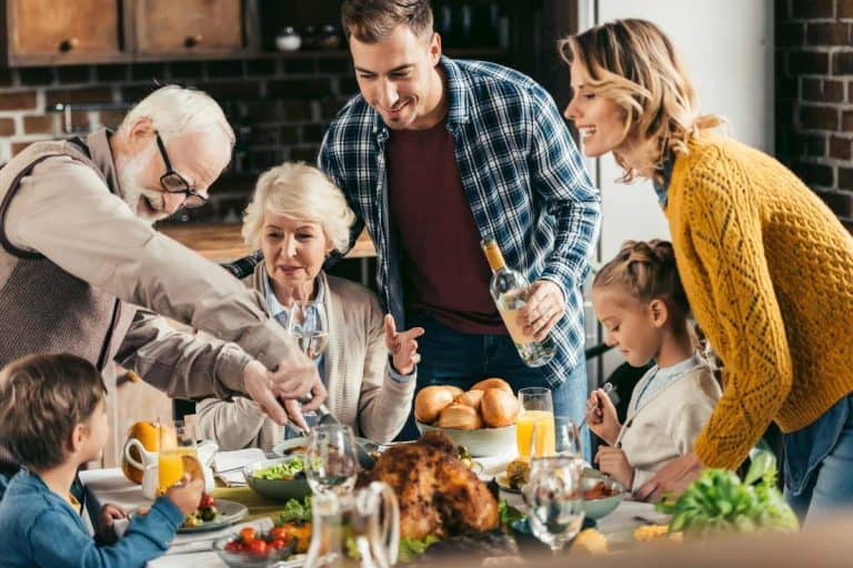 Family carving a turkey around the Thanksgiving dinner table
