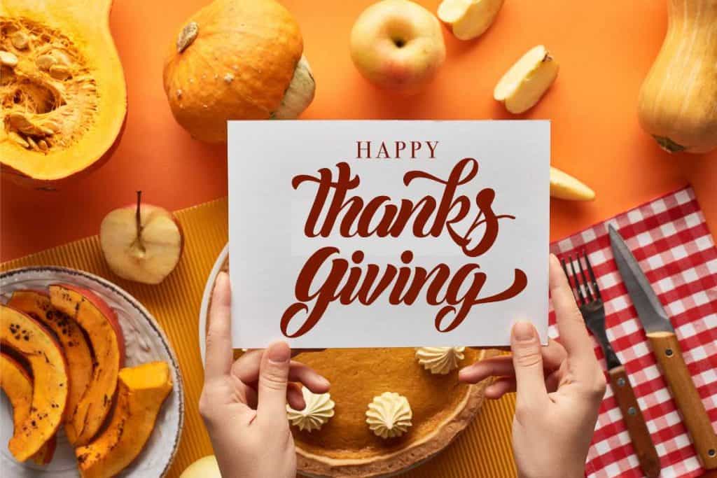 Happy Thanksgiving written on a card being held up over a Thanksgiving table
