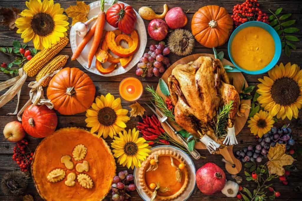 Thanksgiving feast on a table as seen from above. Lots of vegetables and pies and candles and sunflowers are all around the table