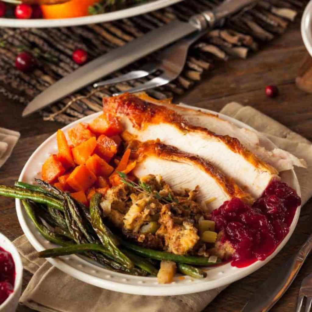 Plate of Thanksgiving food including turkey, dressing, sweet potates, green beans and cranberry sauce.