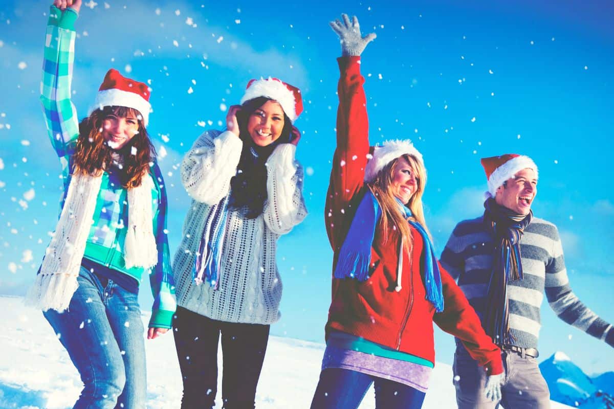 4 College kids out in the snow wearing santa hats and smiling
