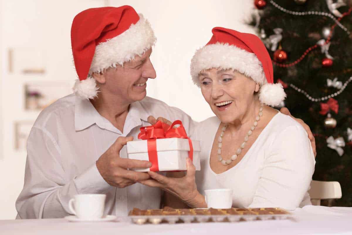 Two older adults exchange a gift in front of the Christmas tree