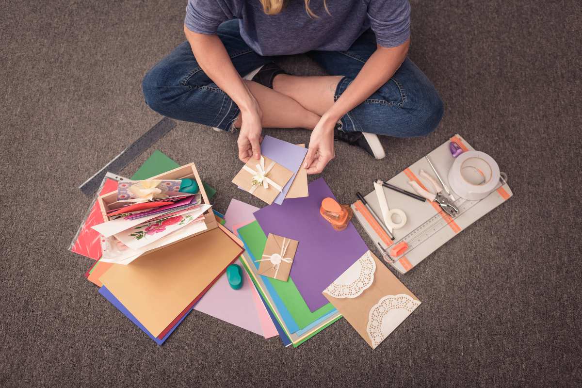 A woman sitting in the floor making paper crafts with all her supplies surrounding her.