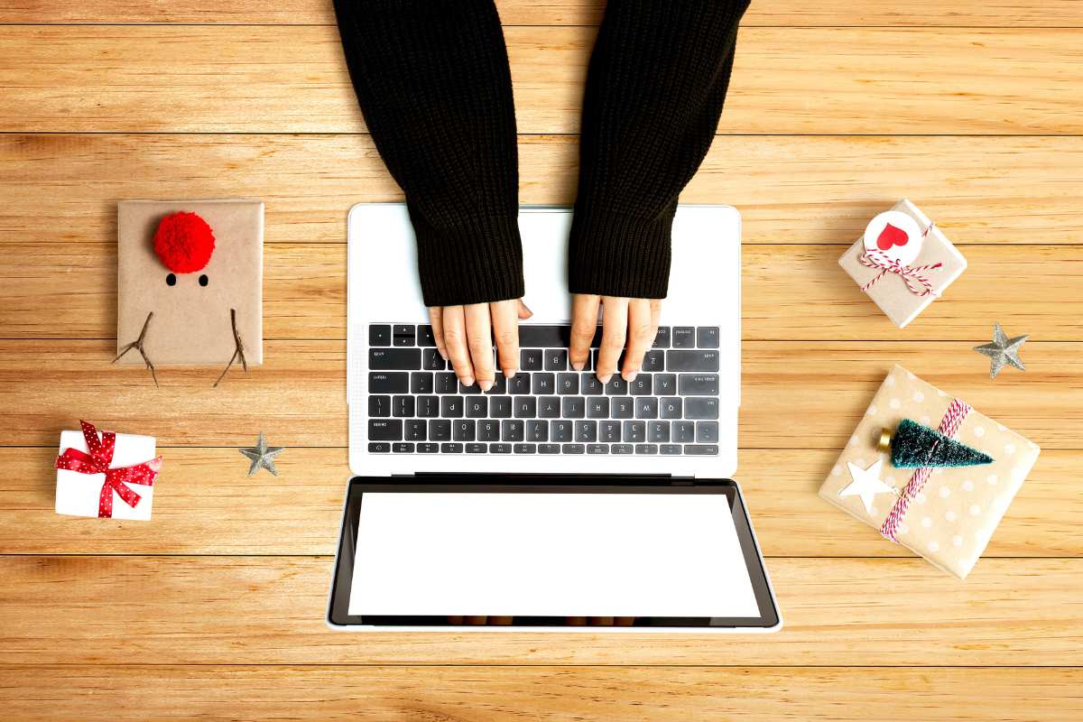 Woman's hands typing on a laptop keyboard with Christmas gifts around her on the table