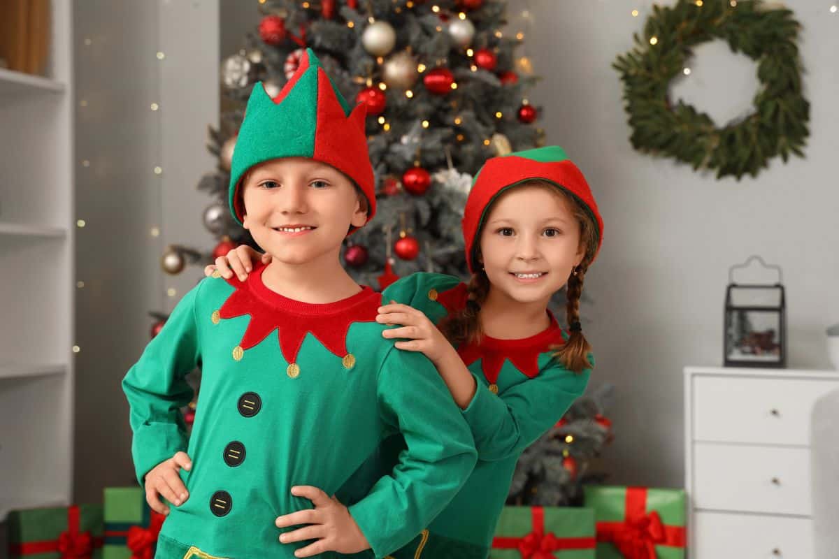 Two young kids dressed as elves in front of the Christmas tree