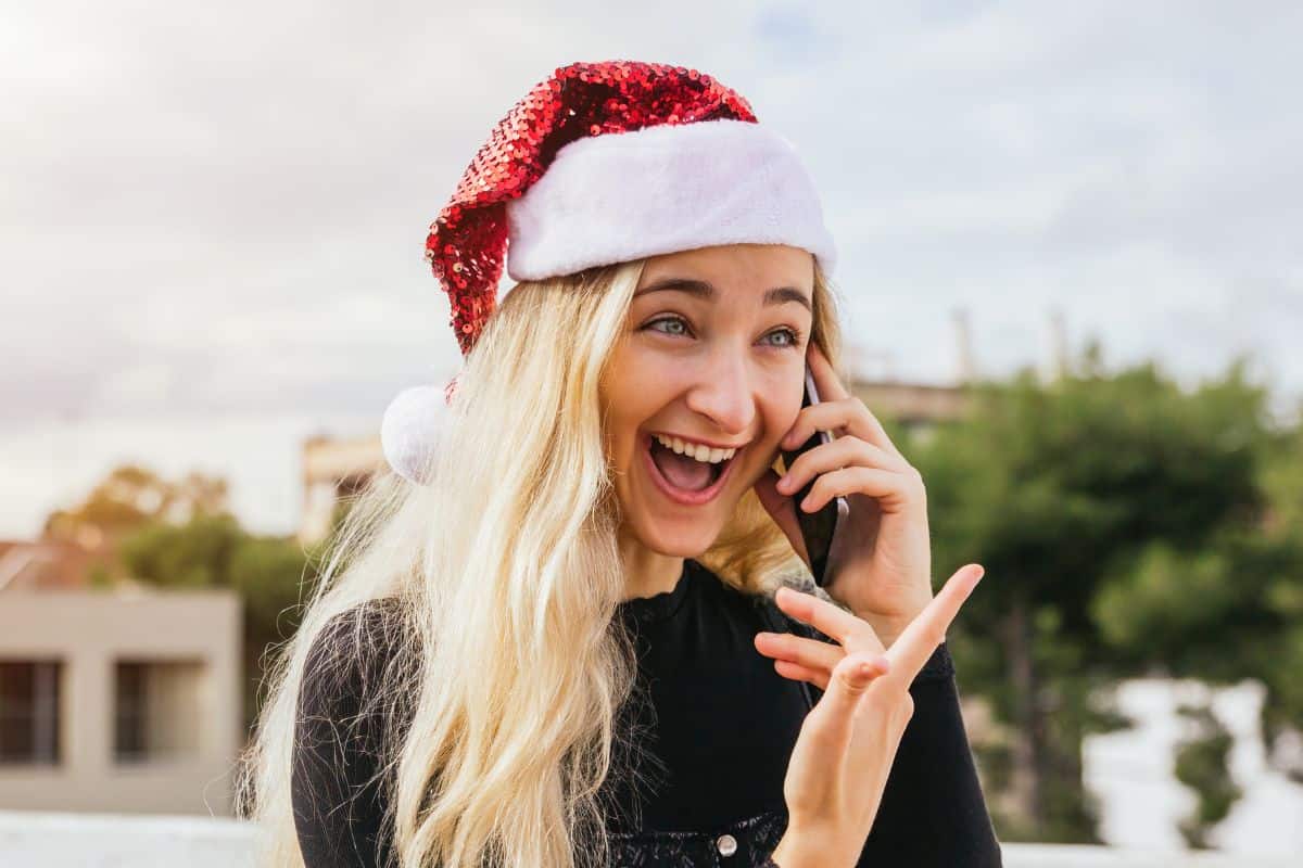 Blonde teenage girl with a sequined Santa hat on talking on the phone and smiling