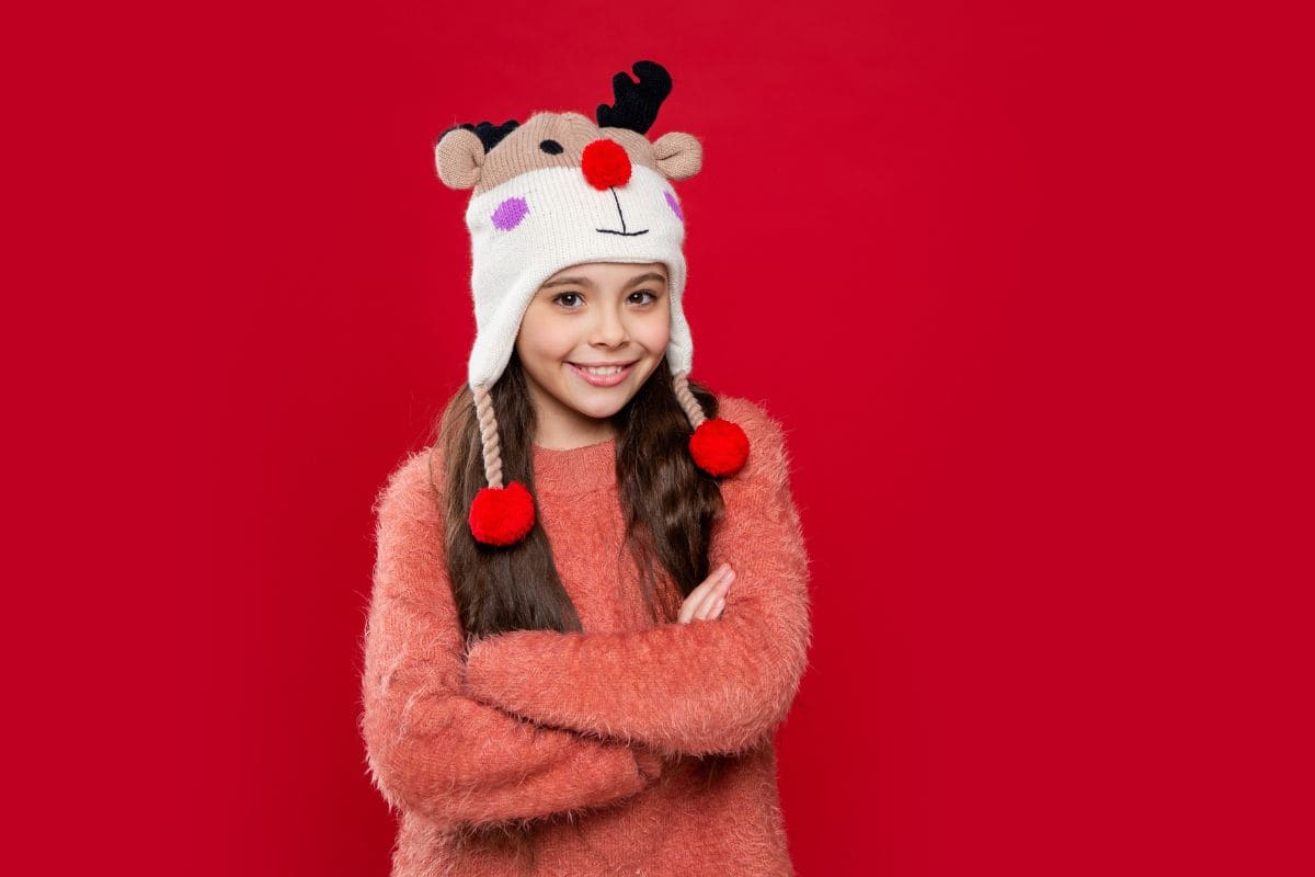 Tween girl smiling at the camera and wearing a rudolph hat with her arms crossed
