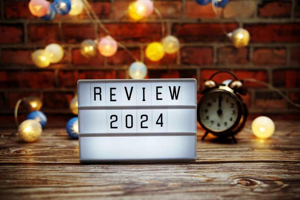 Light up board that says "Review 2024" on a desk with a clock and twinkly lights behind it