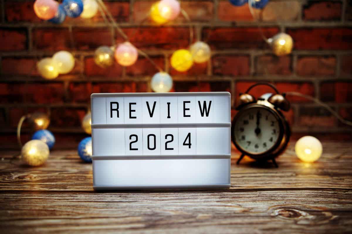 Light up board that says "Review 2024" on a desk with a clock and twinkly lights behind it