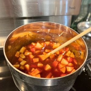 A sauce pan with chunks of apple and bbq sauce with a wooden spoon for stirring
