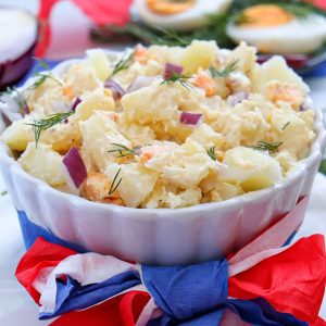 Creamy Summertime potato salad in a white bowl with red, white and blue ribbons tied around it